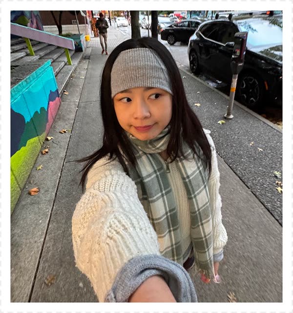 Smiling young woman with long black hair, wearing a fluffy blue cardigan and white top, sits against a plain white background. The tone is cheerful and warm.